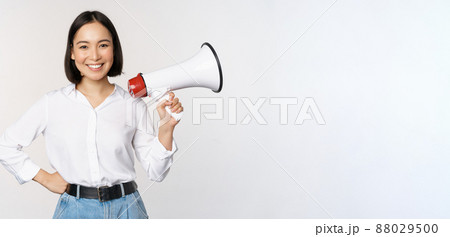 Smiling young asian woman posing with megaphone, concept of news, announcement and information, standing over white background 88029500