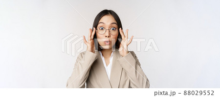 Portrait of asian businesswoman in glasses, looking surprised amazed at camera, standing in suit over white background Portrait of asian businesswoman in glasses, looking surprised amazed at camera, standing in suit over white background 88029552