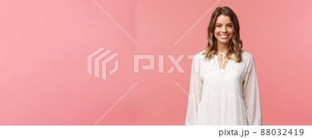 Spring, beauty and women concept. Portrait of tender feminine blonde girl with white beaming smile standing in light cute dress over pink background with happy attitude, positive emotions 88032419