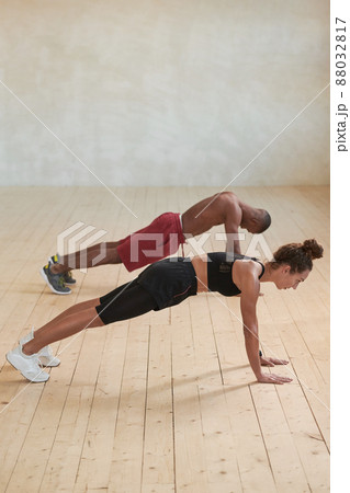 Vertical studio shot of sporty young Black man and Caucasian woman doing strengthening plank exercise in loft studio room 88032817