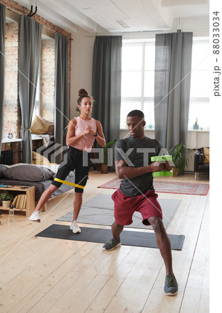 Vertical shot of sporty couple doing strengthening exercises in loft living room using resistance band and dumbbells Vertical shot of sporty couple doing strengthening exercises in loft living room using resistance band and dumbbells 88033034