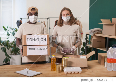 Medium portrait of young adult man and woman wearing protective masks and gloves working together in charity looking at camera 88033111