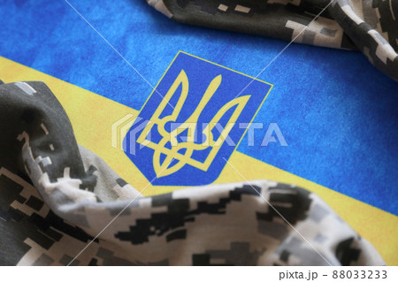 Ukrainian flag and coat of arms with fabric with texture of pixeled camouflage. Cloth with camo pattern in grey, brown and green pixel shapes with Ukrainian trident sign Ukrainian flag and coat of arms with fabric with texture of pixeled camouflage. Cloth with camo pattern in grey, brown and green pixel shapes with Ukrainian trident sign 88033233