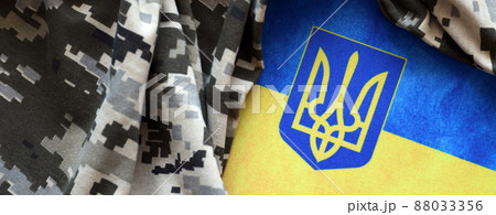 Ukrainian flag and coat of arms with fabric with texture of pixeled camouflage. Cloth with camo pattern in grey, brown and green pixel shapes with Ukrainian trident sign Ukrainian flag and coat of arms with fabric with texture of pixeled camouflage. Cloth with camo pattern in grey, brown and green pixel shapes with Ukrainian trident sign 88033356