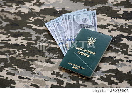 Ukrainian military ID and US dollar bills on fabric with texture of pixeled camouflage. Cloth with camo pattern in grey, brown and green pixel shapes with Ukrainian army personal token. Ukrainian military ID and US dollar bills on fabric with texture of pixeled camouflage. Cloth with camo pattern in grey, brown and green pixel shapes with Ukrainian army personal token. 88033600