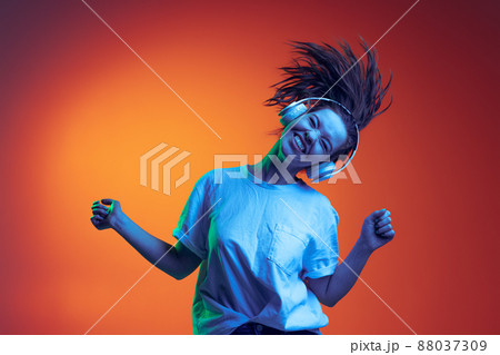 Young happy girl emotively listening to music in headphones isolated over gradient red yellow background in neon ligh. Young happy girl emotively listening to music in headphones isolated over gradient red yellow background in neon ligh. 88037309