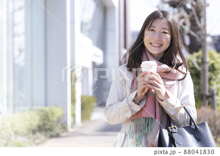 コーヒーを飲みながら笑顔で歩く女性 88041830