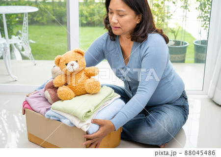 Holding clothing donation box with used clothes and doll at home to support help for poor people in the world. 88045486