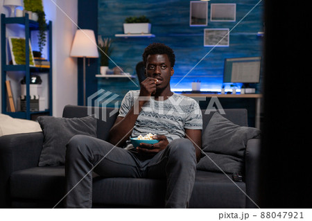 Relaxed young adult resting on couch watching football game on television spending evening alone at home in living room. Guy holding popcord bowl looking at comedy movie on tv enjoying free time 88047921