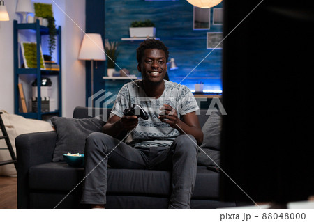 Happy excited african american gamer playing virtual video games using wireless joystick winning online gaming tournament. Winner player relaxing on couch in living room enjoying leisure time 88048000