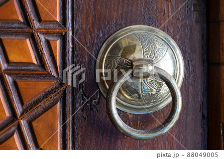 Closeup of antique copper ornate door knocker over an aged wooden door Closeup of antique copper ornate door knocker over an aged wooden door 88049005