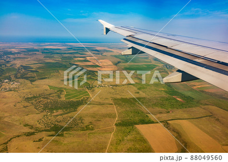 View of airplane wing, blue skies and green land during landing. Airplane window view. View of airplane wing, blue skies and green land during landing. Airplane window view. 88049560