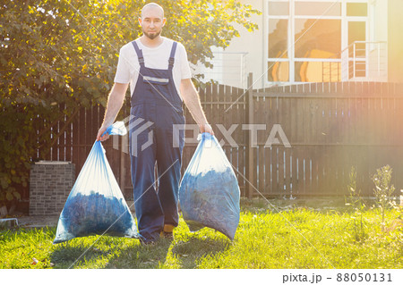 The gardener smiling and removes the bags of compost. Light. Blue uniform The gardener smiling and removes the bags of compost. Light. Blue uniform 88050131