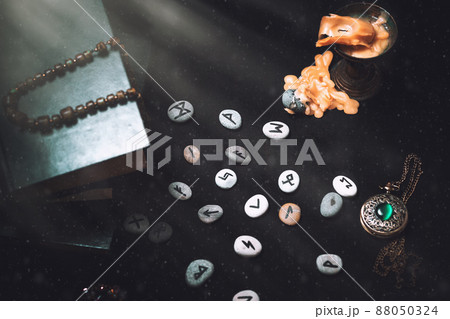 Astrology and esotericism. On a black background lie fortune-telling runes, a book, an amulet, and a candle. Light. Top view Astrology and esotericism. On a black background lie fortune-telling runes, a book, an amulet, and a candle. Light. Top view 88050324