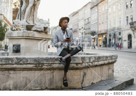 African american man sitting outdoors and using smartphone African american man sitting outdoors and using smartphone 88050483