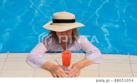 smiling blonde woman in straw hat relaxes and drinks orange cocktail near the swimming pool on a 88051054