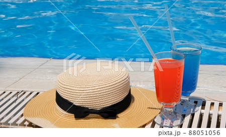 Two colorful cocktail glasses pink and blue, sun hat on the edge of the swimming pool, close up 88051056