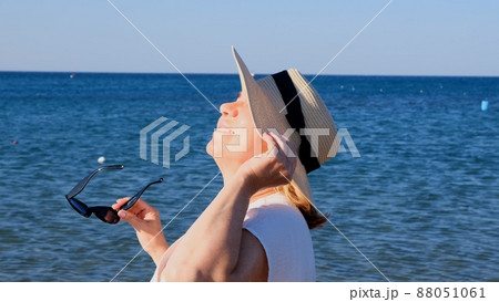 happy 50 year old woman in straw hat and sunglasses enjoying the sun against the blue sea background 88051061