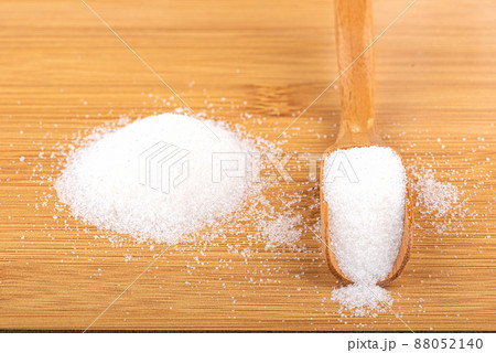 Wooden scoop with white sugar and a pile of sugar on a wooden background. 88052140