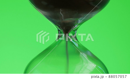 Hourglass on green background. Sand is pouring from one part to another. Time and transience concept. Hourglass on green background. Sand is pouring from one part to another. Time and transience concept. 88057057
