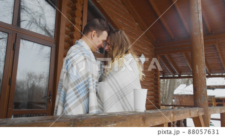A guy and a girl wrapped in a blanket, standing at a wooden house in winter. Romance A guy and a girl wrapped in a blanket, standing at a wooden house in winter. Romance 88057631