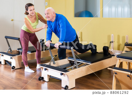 Senior man practicing pilates on reformer under supervision of female trainer 88061292