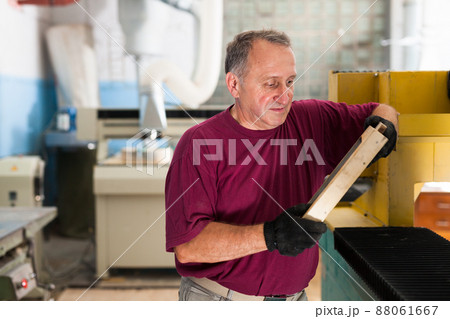 Elderly worker checks metal detail on a wooden sample 88061667
