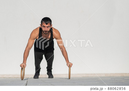 A man in black sportswear doing ring push-ups outdoors. A man in black sportswear doing ring push-ups outdoors. 88062856