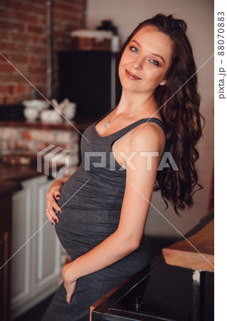 a beautiful pregnant woman in a gray dress in the kitchen in the loft style. a beautiful pregnant woman in a gray dress in the kitchen in the loft style. 88070883
