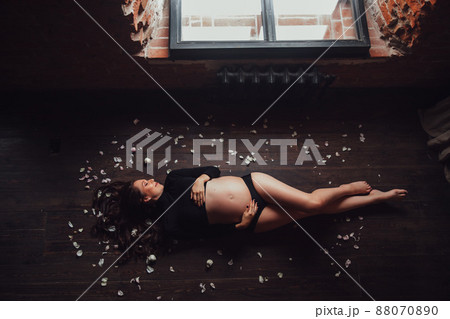 pregnant woman in black with naked belly on floor in petals of white roses pregnant woman in black with naked belly on floor in petals of white roses 88070890