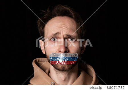 Close-up portrait of young emotive man with three colors duct tape over his mouth isolated on dark background. Censorship, freedom of speech concept. Close-up portrait of young emotive man with three colors duct tape over his mouth isolated on dark background. Censorship, freedom of speech concept. 88071782