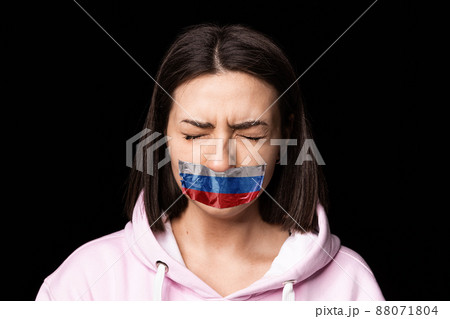 Front camera view. Portrait of young upset girl with three colors duct tape over her mouth isolated on dark background. Censorship, freedom of speech concept. 88071804