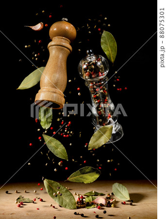 Two spice mills with peppercorns and laurel bay leaves on black flying over table. Two spice mills with peppercorns and laurel bay leaves on black flying over table. 88075301