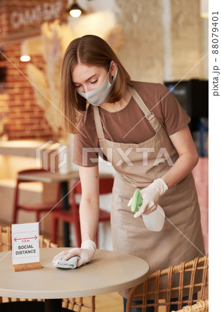 Medium long shot of unrecognizable young waitperson working in modern cafe wiping table with social distance sign on it Medium long shot of unrecognizable young waitperson working in modern cafe wiping table with social distance sign on it 88079401