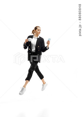 Dynamic portrait of young woman, office worker in black official suit having video call on phone isolated over white studio background 88080848