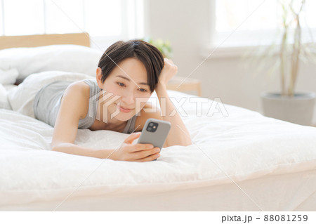 ベッドに寝転んでスマホを見る女性 ベッドに寝転んでスマホを見る女性 88081259