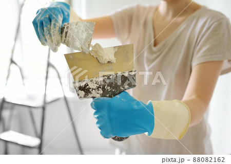 Young female worker preparing putty for the wall repair. Close-up view of spreading plaster on metal spatula. Do it yourself. 88082162