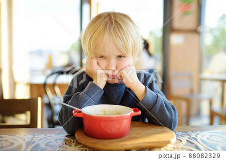 Little child sitting the table in cafe or restaurant and doesn't want to eat. Healthy food. Kids diet. Poor appetite. 88082329