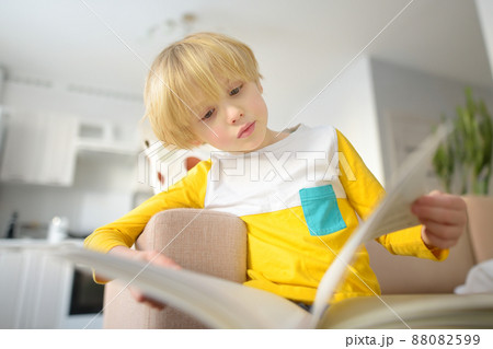 Little boy is reading a book at home. Preschool child is watching at pictures in a book with a fairy tale. A child of primary school age is learning to read. Little boy is reading a book at home. Preschool child is watching at pictures in a book with a fairy tale. A child of primary school age is learning to read. 88082599