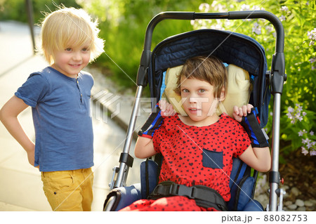Little boy and disabled girl in wheelchair playing together in summer park. Child cerebral palsy. Family with disabled kid. Accessible urban environment for disabled person. Kids with special needs. Little boy and disabled girl in wheelchair playing together in summer park. Child cerebral palsy. Family with disabled kid. Accessible urban environment for disabled person. Kids with special needs. 88082753