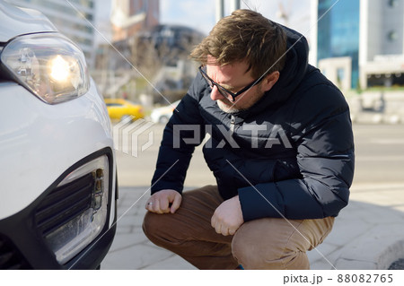 Man is watching broken automobile headlight. Destroyed front light on the left side. Car crash or accident. Insurance, repair. Man is watching broken automobile headlight. Destroyed front light on the left side. Car crash or accident. Insurance, repair. 88082765