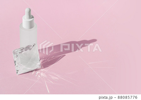 Serum cosmetic bottle mockup with quartz transparent prism crystal on pink background, with glass prism refracting light effects and rays of light. . Serum cosmetic bottle mockup with quartz transparent prism crystal on pink background, with glass prism refracting light effects and rays of light. . 88085776