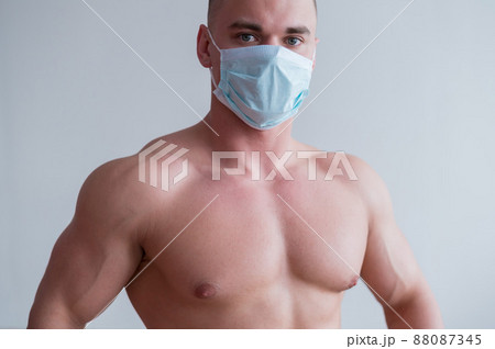 Male bodybuilder in a medical mask with muscular bare chest. The guy goes in for sports in quarantine. Respiratory protection. 88087345