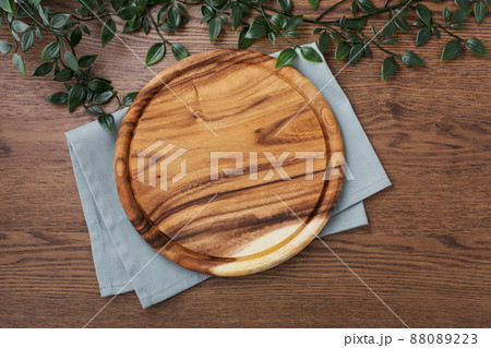 Wood plate with blue napkin on dark wooden table background, board for pizza, cutting board Wood plate with blue napkin on dark wooden table background, board for pizza, cutting board 88089223