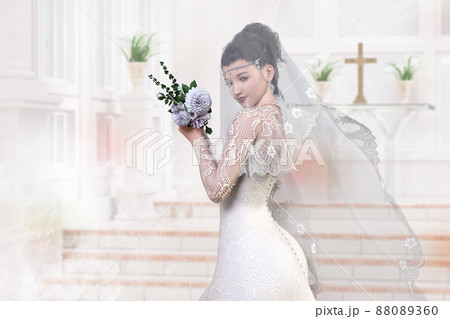 ベールをつけた純白のウエディングドレスを着た花嫁がウエディングチャペルの祭壇近くに立つ 88089360
