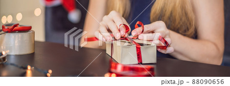 Young woman is packing presents. Present wrapped in craft paper with a red and gold ribbon for christmas or new year. Woman makes an advent calendar for her child BANNER, LONG FORMAT Young woman is packing presents. Present wrapped in craft paper with a red and gold ribbon for christmas or new year. Woman makes an advent calendar for her child BANNER, LONG FORMAT 88090656