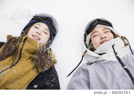 雪の降る中ゲレンデに寝転がるスノボ女子 88092561