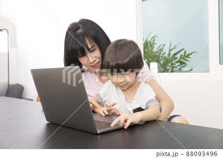 Asian woman with a child works on computer. Concept of work from home and home family education. Mom and son are working on a laptop at home. 88093496