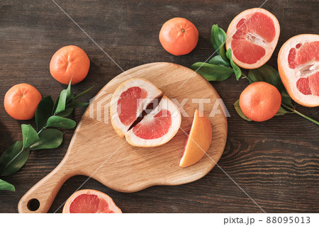 High angle view of two parts of ripe grapefruit on wooden board surrounded citrus fruits and leaves on table 88095013