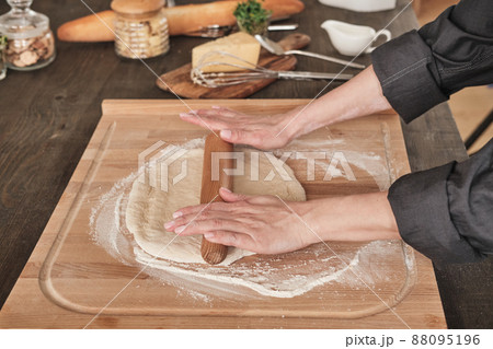 Close-up of unrecognizable woman in black shirt using rolling pin while rolling dough on wooden board Close-up of unrecognizable woman in black shirt using rolling pin while rolling dough on wooden board 88095196